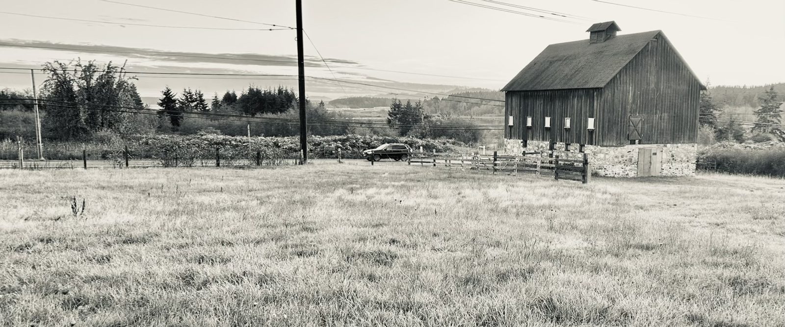 A weathered barn and open pasture on Whidbey Island at dusk, in soft black and white